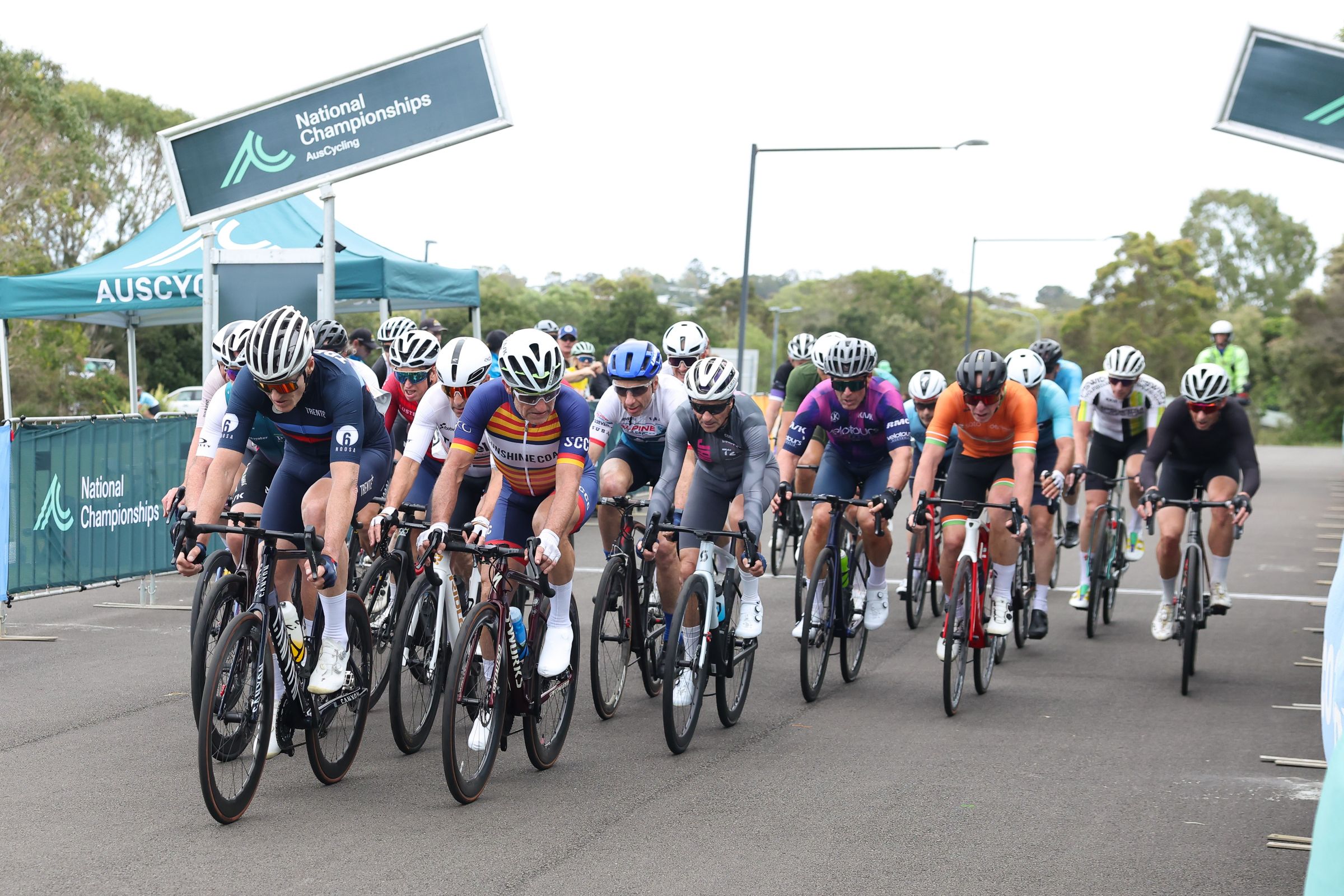 Masters road cyclists competing in a peloton passing signage for AusCycling Junior & Masters Road National Championships